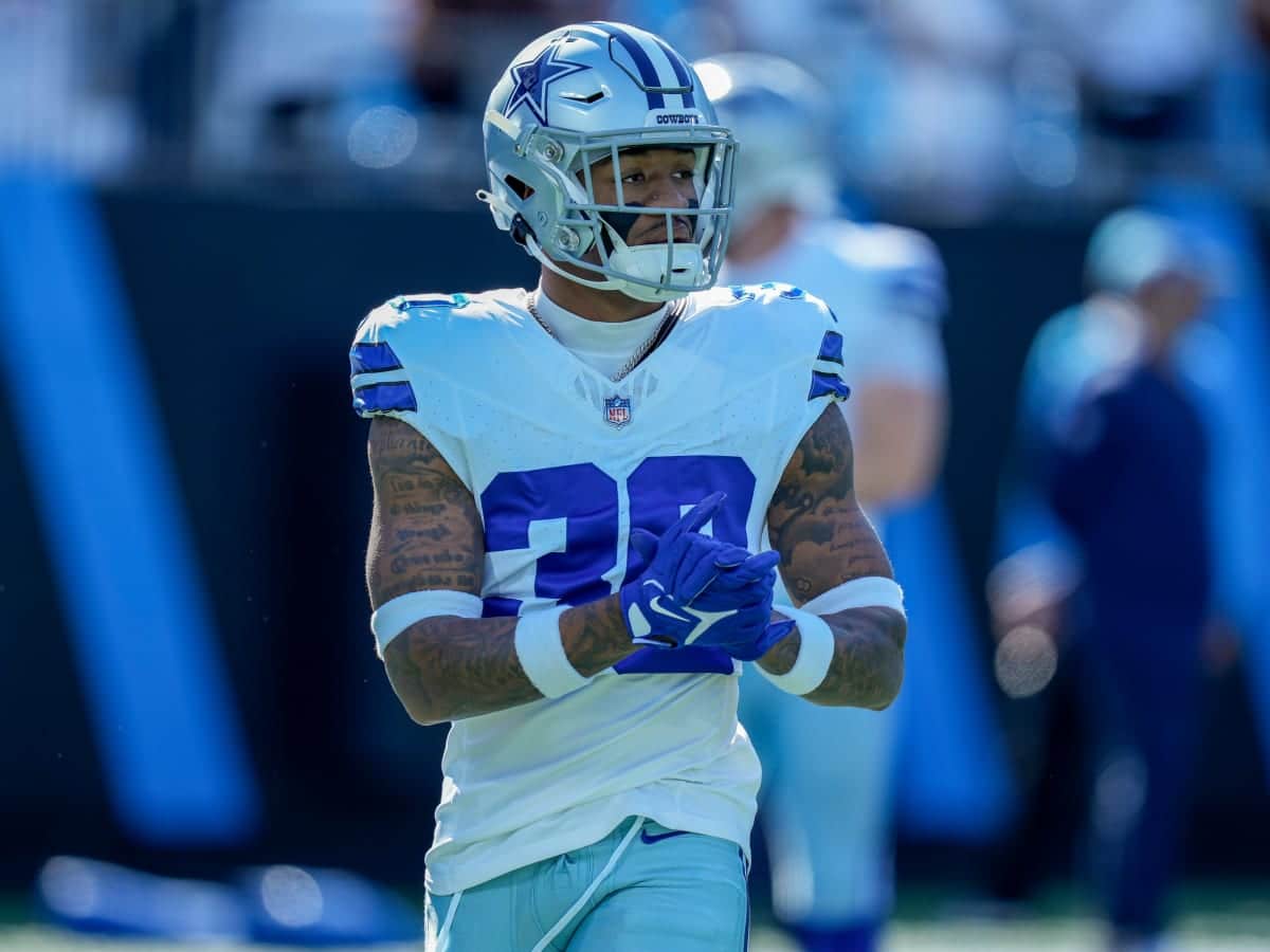 Football player in a Dallas Cowboys uniform stands on the field, wearing a helmet and gloves. Safety Juanyeh Thomas surveys the scene, ready for action.
