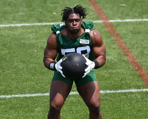 A football player wearing a green jersey holds a medicine ball during a training session on a grass field.
