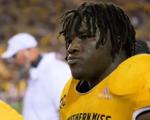 A football player in a yellow "Southern Miss" jersey stands on the sidelines during a game.