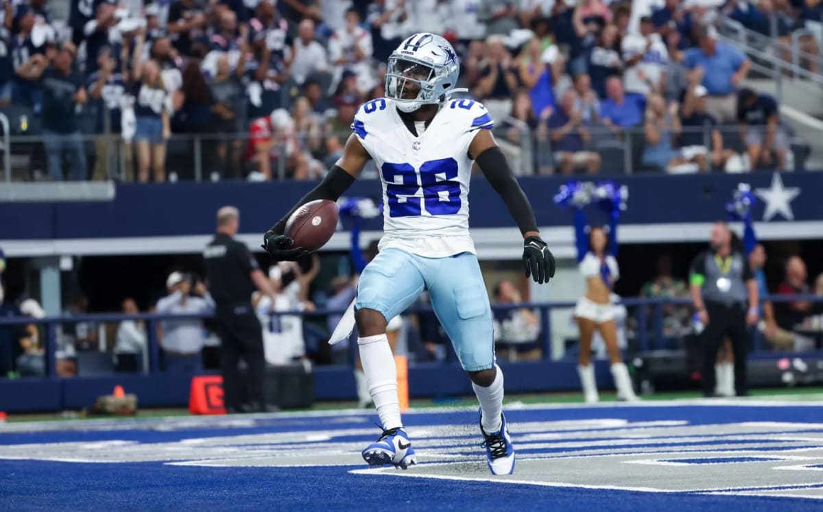 A football player in a white and blue uniform celebrates in the end zone with a football, while the crowd cheers.