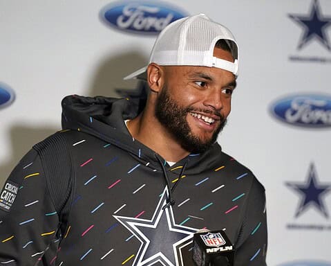 A man in a hoodie and cap stands in front of a backdrop with Ford and Dallas Cowboys logos, smiling.