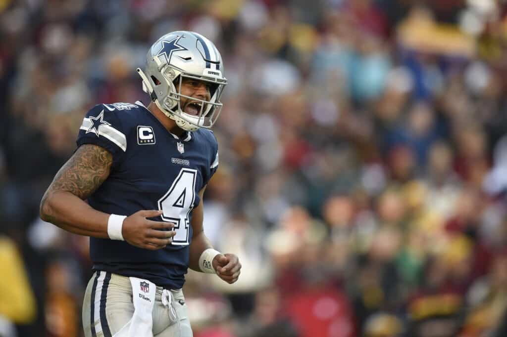 Dallas Cowboys football player wearing jersey number 4, celebrating on the field during a game, with a blurred crowd in the background.