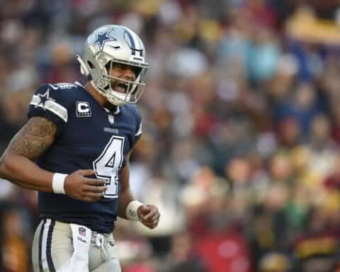 Dallas Cowboys football player wearing jersey number 4, celebrating on the field during a game, with a blurred crowd in the background.