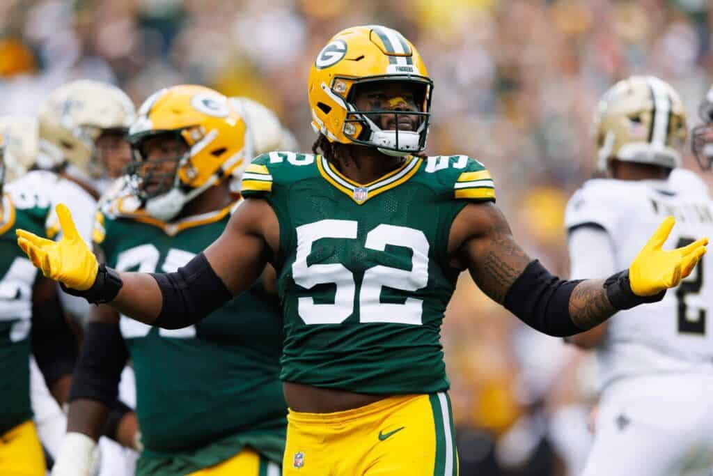 Green Bay Packers player wearing jersey number 52 with arms outstretched during game, surrounded by teammates in football stadium.