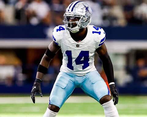 Joueur de football américain des Dallas Cowboys en position de défense sur le terrain, portant un uniforme blanc et bleu avec le numéro 14, lors d'un match de NFL.