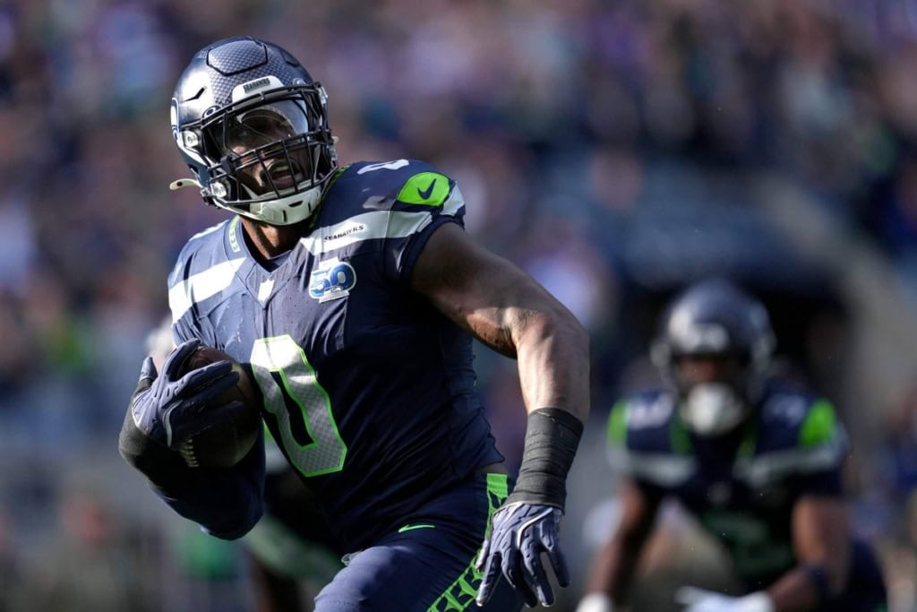 NFC West Seattle Seahawks football player running with ball during NFL game, team in blue and green uniform, stadium crowd in background.