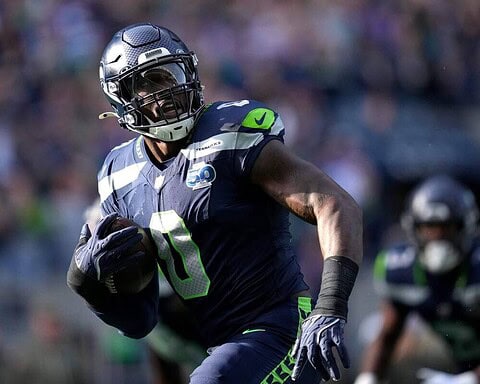 NFC West Seattle Seahawks football player running with ball during NFL game, team in blue and green uniform, stadium crowd in background.