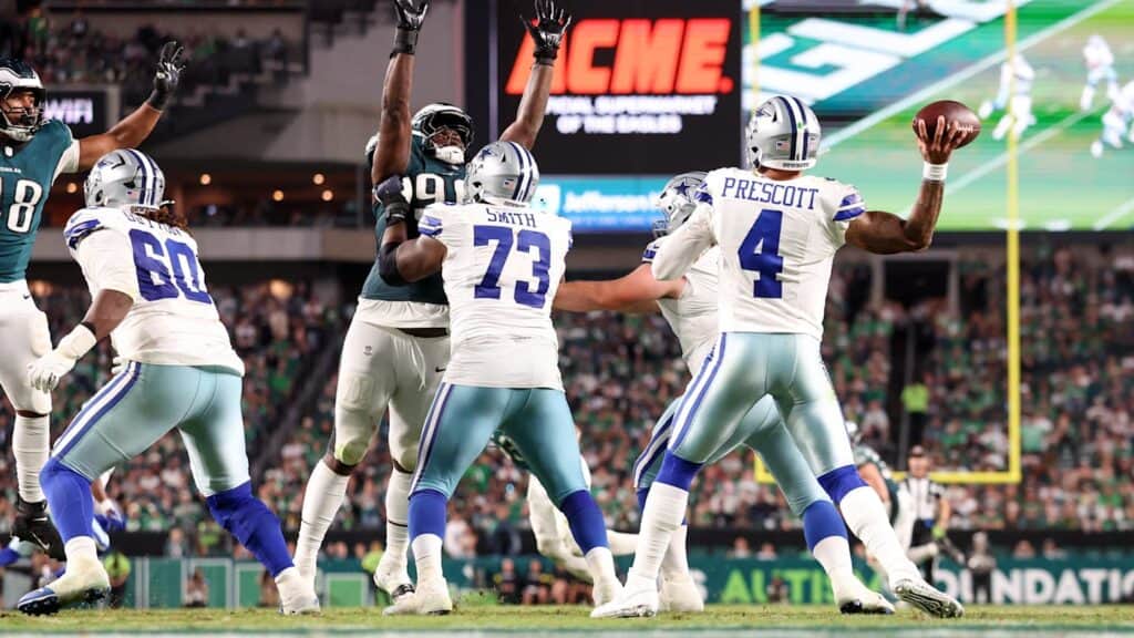 Bold black NFL action during a Dallas Cowboys vs. Philadelphia Eagles football game with quarterback Dak Prescott preparing to throw the football on the field.