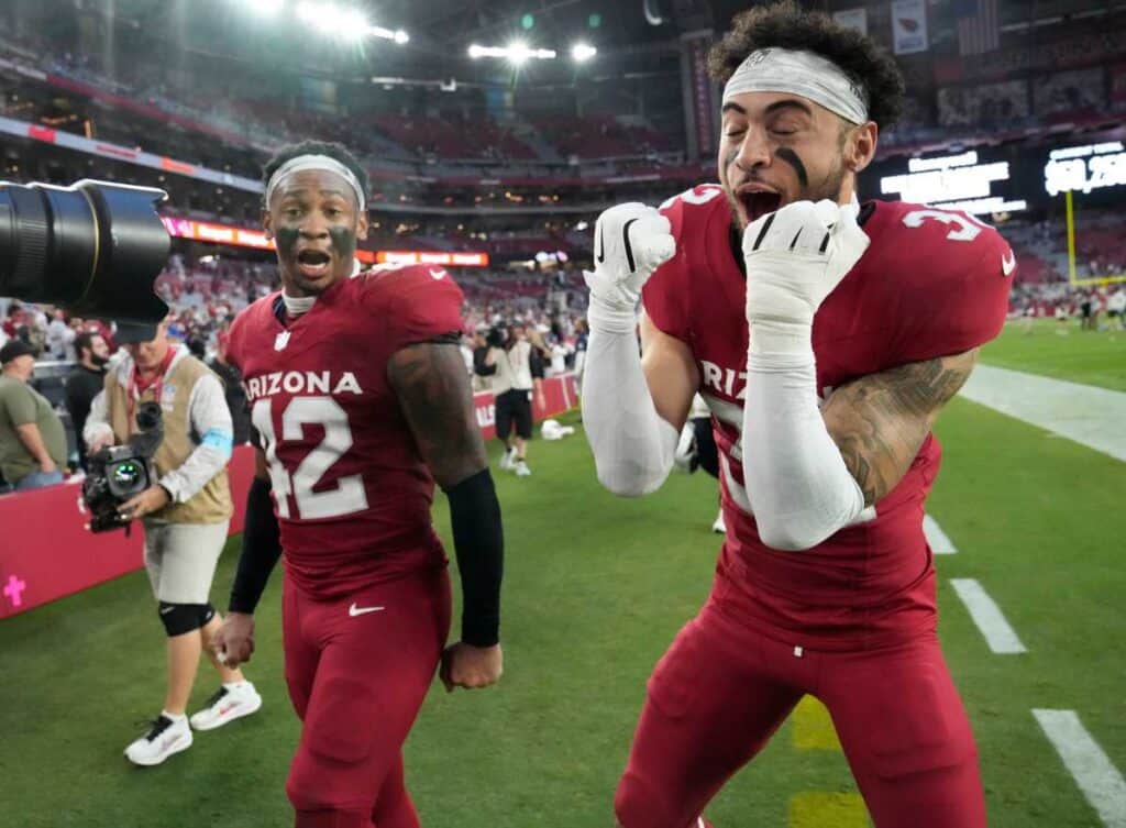 Excited Arizona Cardinals football players celebrating on the field after a victory at State Farm Stadium. Fans and media surround the players, capturing moments of team success and sports enthusiasm at an NFL game.