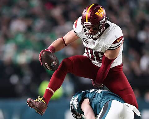 Football player in action during game, wearing Washington Football Team uniform, tackling opponent on field, crowd in background, highlighting NFL football, athlete performance, sportsmanship.