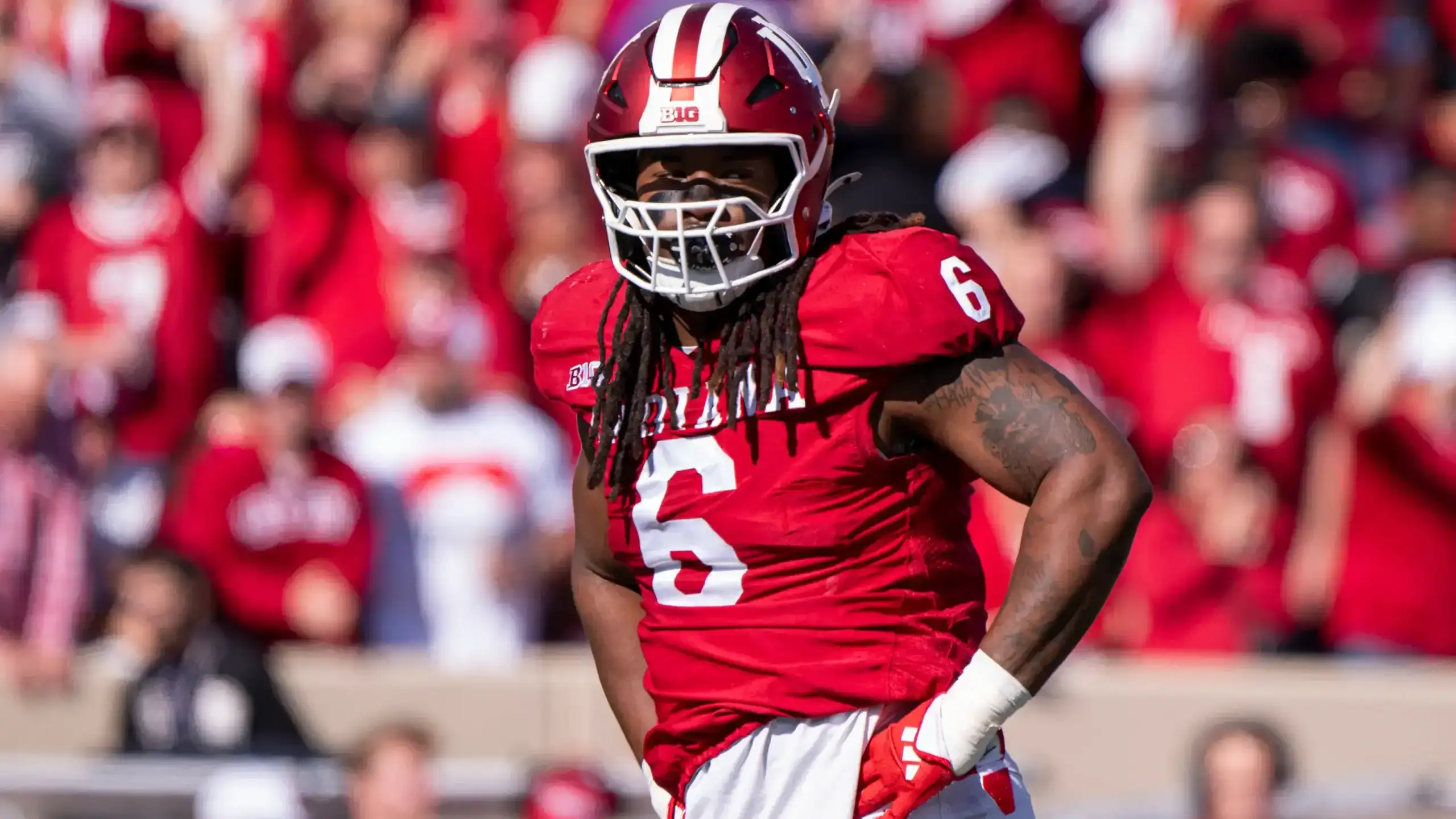Indiana Hoosiers football player Mikail Kamara, wearing a red No. 6 jersey and helmet, stands on the field with hands on hips during a daytime game as fans fill the stands behind him.