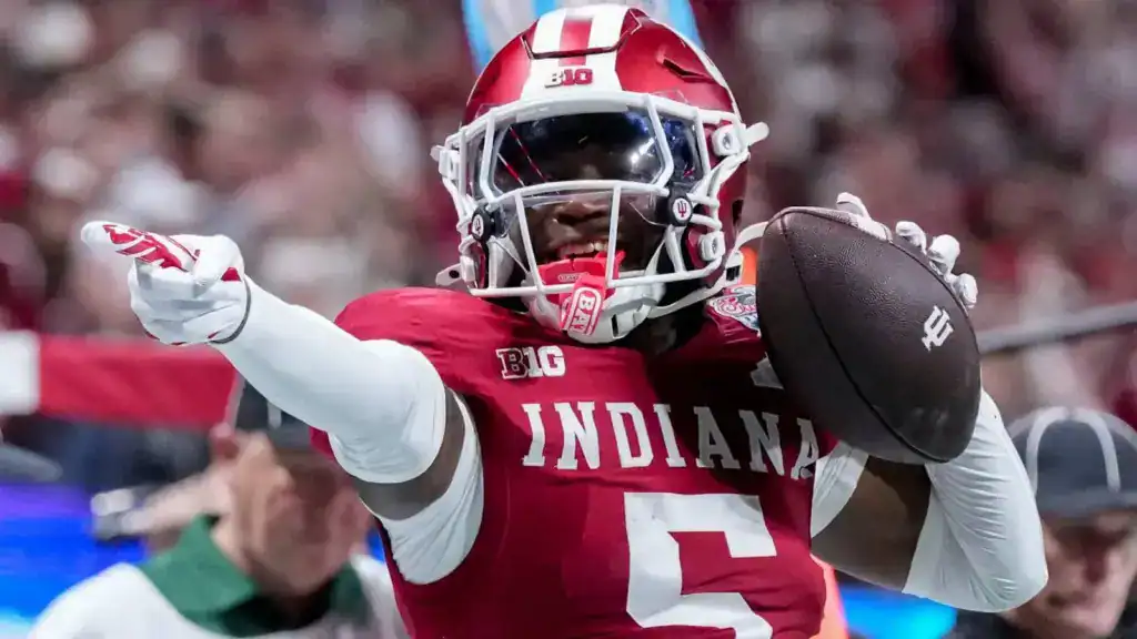  Indiana football cornerback, D’Angelo Ponds, in a red jersey throwing a pass while pointing downfield, wearing a white helmet and holding the ball mid-motion during live action.
