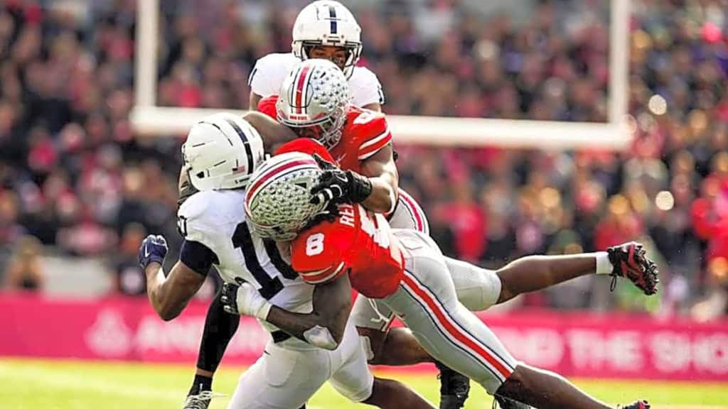 Ohio State defenders, Arvell Reese and Sonny Styles, dives to make a tackle on a Penn State ball carrier as teammates converge during a college football game.