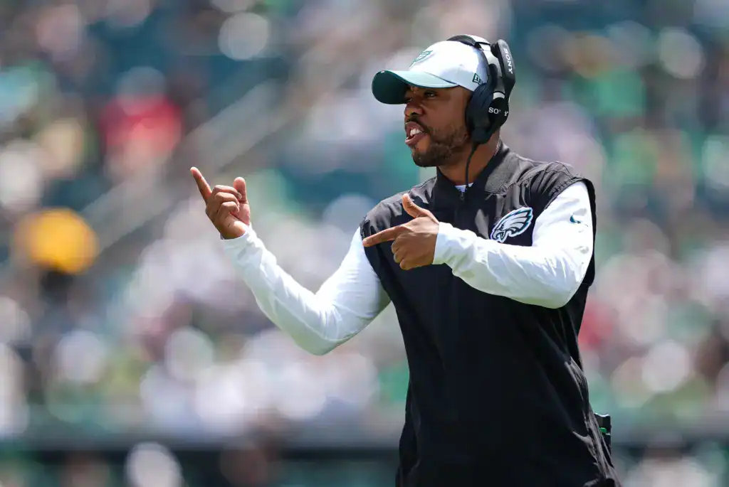 Philadelphia Eagles coach, Christian Parker, wearing a headset and team vest gestures with both hands while giving instructions on the sideline during a game.