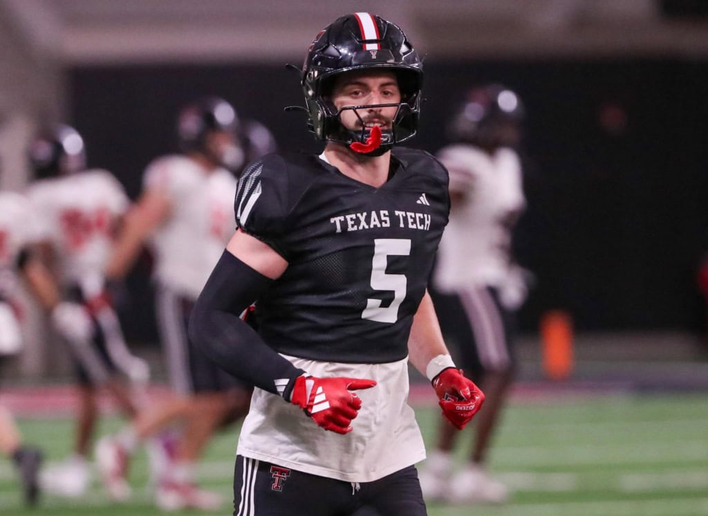 Texas Tech Red Raiders safety, Cole Wisniewski, wearing a black No. 5 jersey jogs on the field during a night game with teammates blurred in the background.