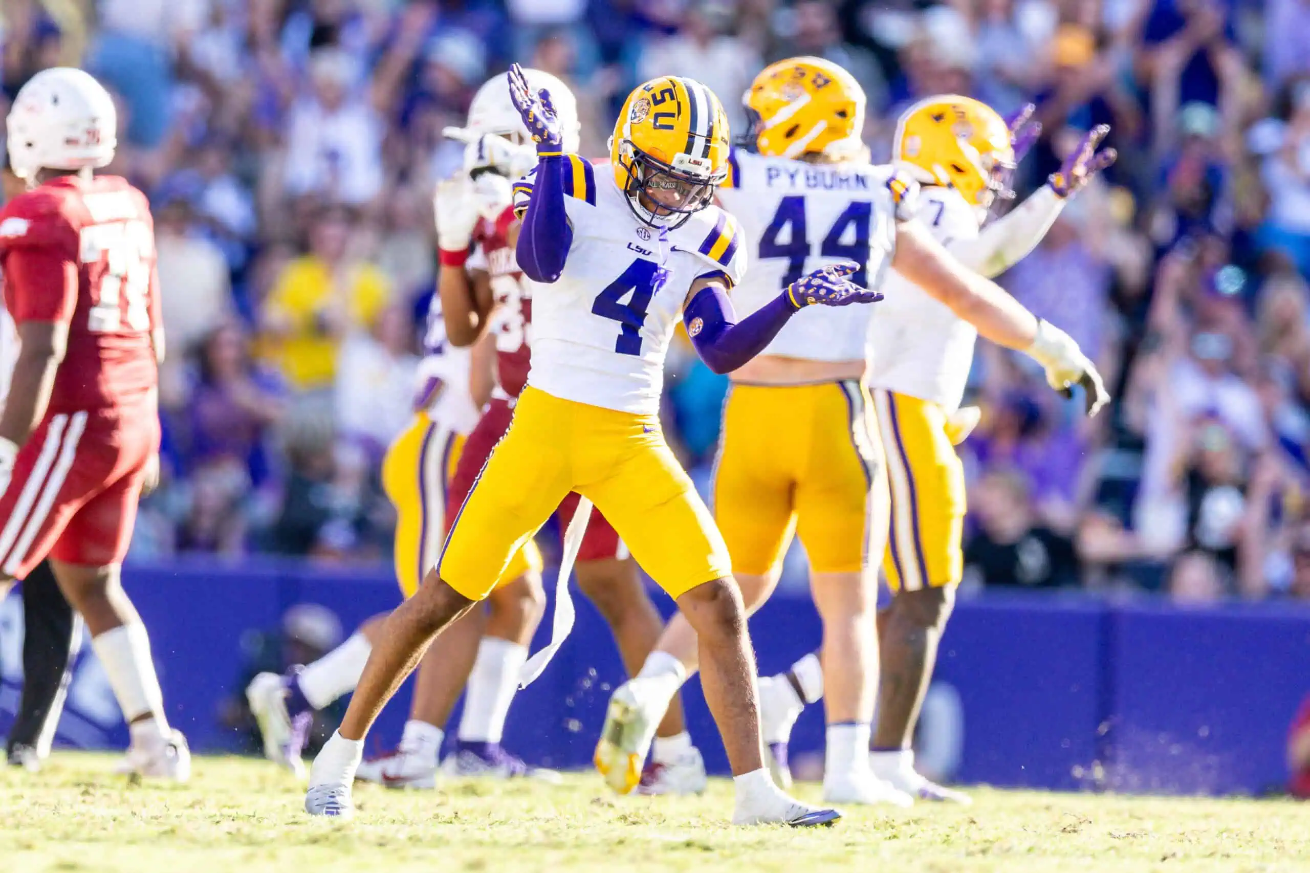 LSU Tigers 2026 NFL Draft prospect wearing a white No. 4 jersey celebrates on the field with an emphatic pose after a big defensive play, with teammates and a packed stadium in the background.
