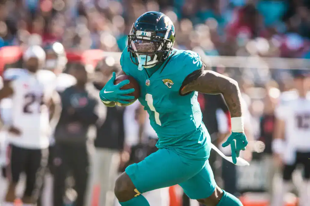 Ranking the 2026 Running Back Tiers: Who Actually Fits the Cowboys? Jacksonville Jaguars running back in a teal No. 1 jersey sprints through traffic during a daytime NFL game, part of a ranking of free agent running backs.