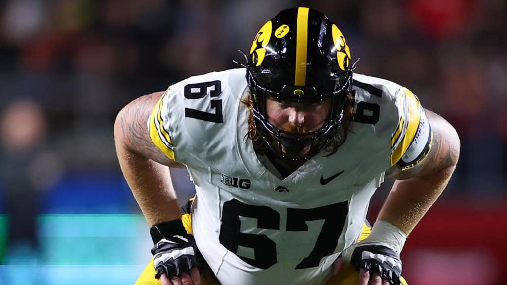 Iowa Hawkeyes offensive lineman wearing a white No. 57 jersey prepares for a snap during a college football game, part of Senior Bowl prospect coverage.
