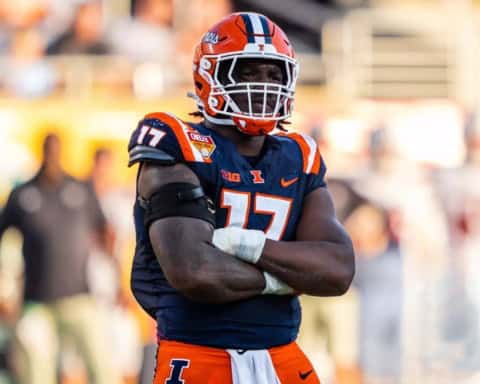 Illinois football player wearing an orange helmet and navy uniform with number 17 stands on the field with arms crossed during a game.