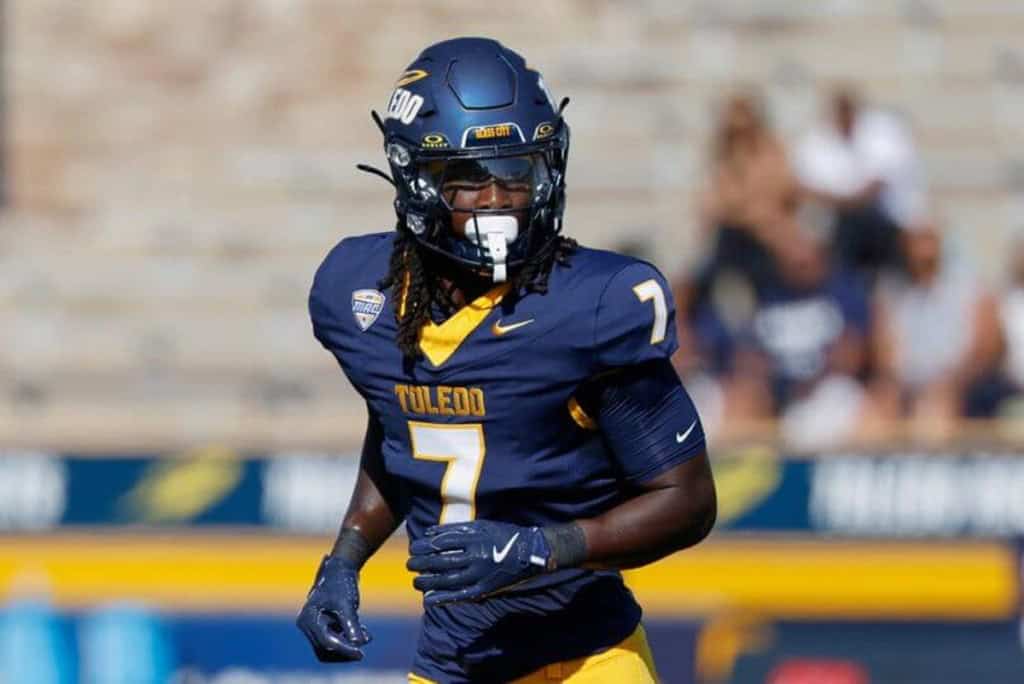 Emmanuel McNeil-Warren in a navy Toledo uniform wearing No. 7 during a college football game, preparing for the snap.