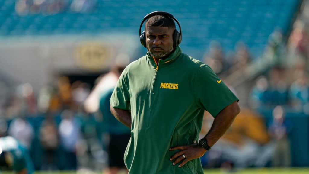 Coach Derrick Ansley on the practice field wearing Packers gear, focused and evaluating players during warmups