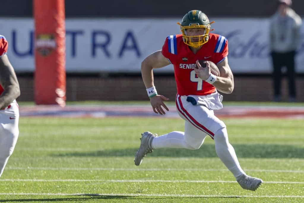 North Dakota State Quarterback wearing a red Senior Bowl jersey sprints downfield with the ball during practice, showing athleticism and mobility.