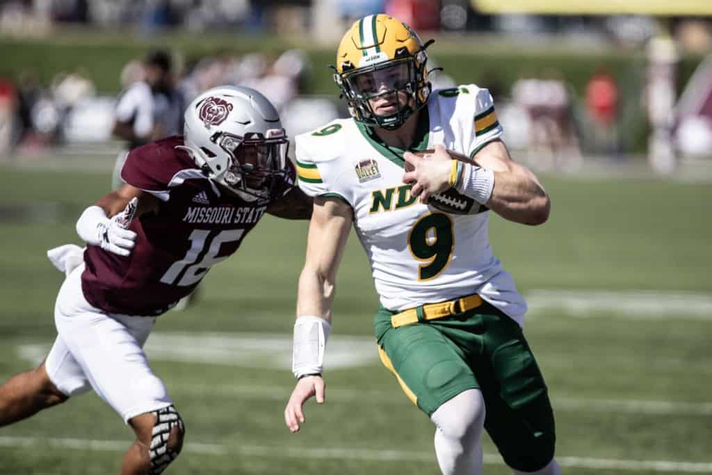 North Dakota State Quarterback runs past a Missouri State defender while carrying the ball during a college football game.