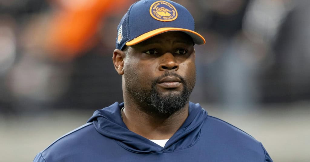 Coach Marcus Dixon wearing a Denver Broncos cap and hoodie, focused during pregame warmups.
