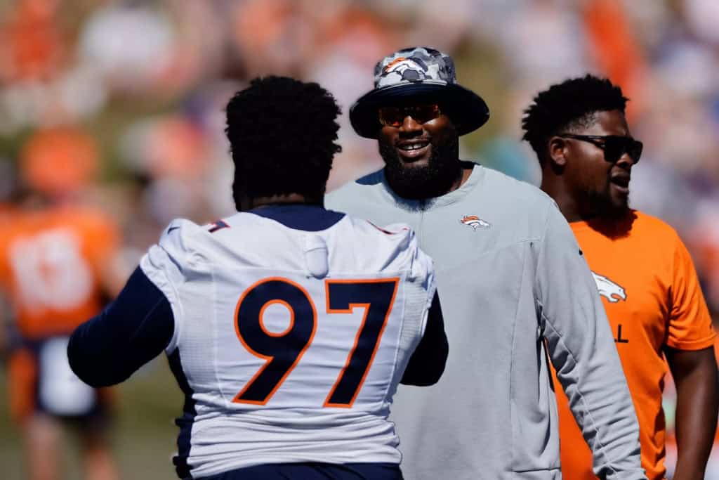 Marcus Dixon smiling while talking with a Denver Broncos player during NFL practice.