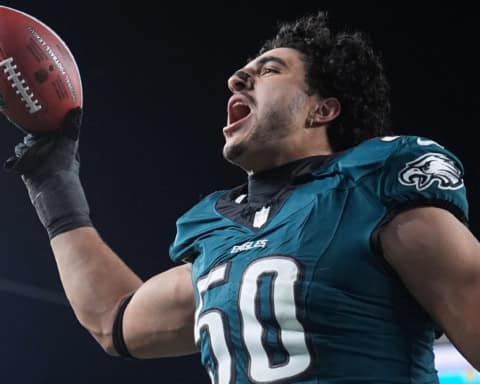 Jaelan Phillips holding a football and celebrating in a Philadelphia Eagles green jersey under stadium lights.