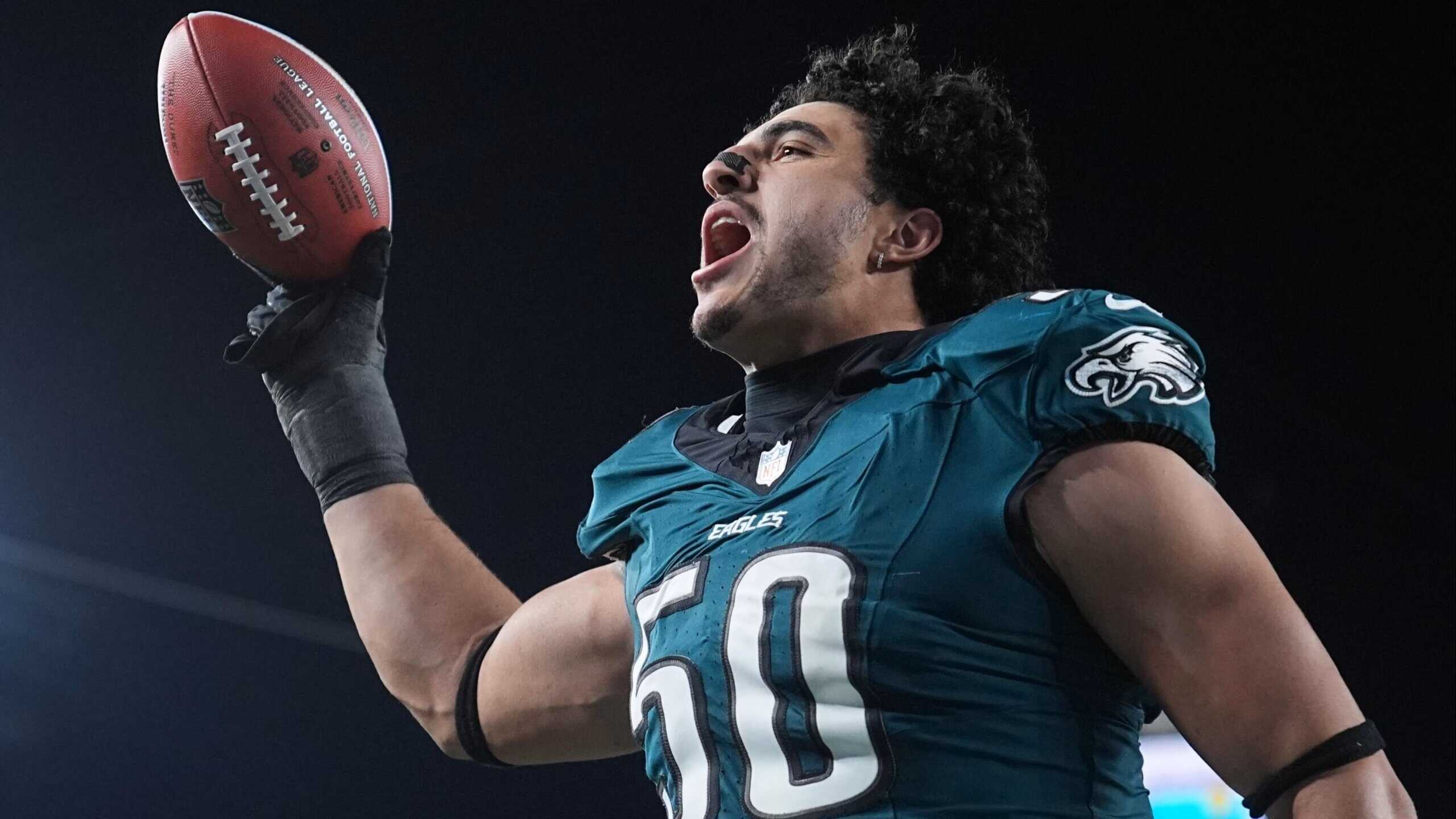 Jaelan Phillips holding a football and celebrating in a Philadelphia Eagles green jersey under stadium lights.