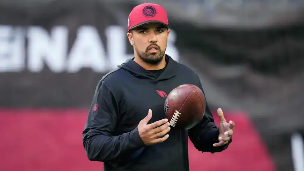 Coach Ryan Smith holding a football during Arizona Cardinals practice, preparing quarterbacks for drills.