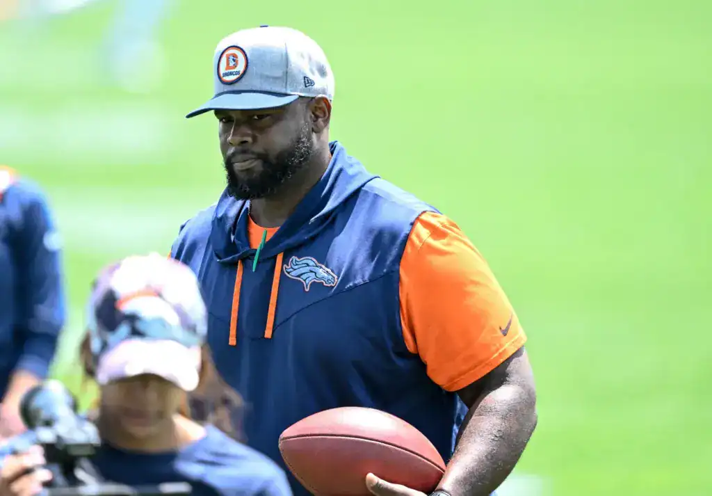 Marcus Dixon holding a football while coaching at Denver Broncos practice on the field.