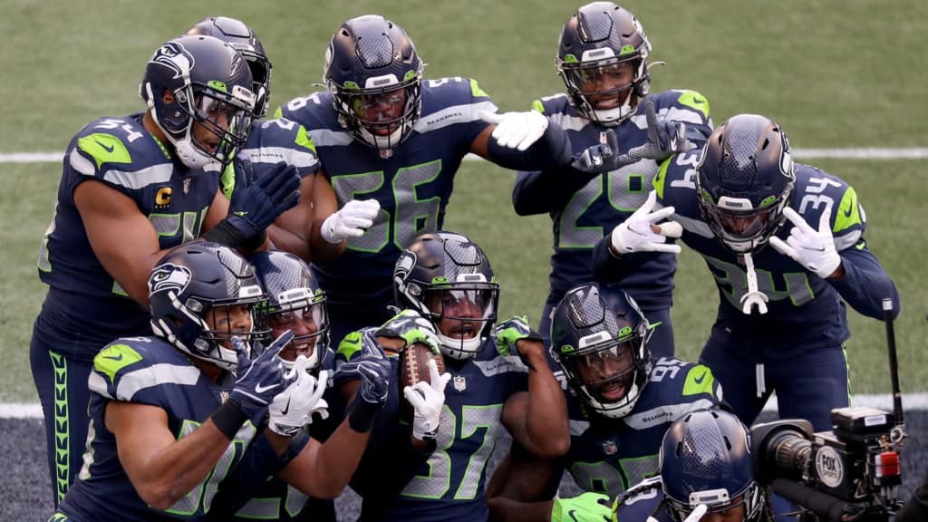Seattle Seahawks defensive unit celebrating a turnover during an NFL game, showcasing team chemistry and aggressive defensive play