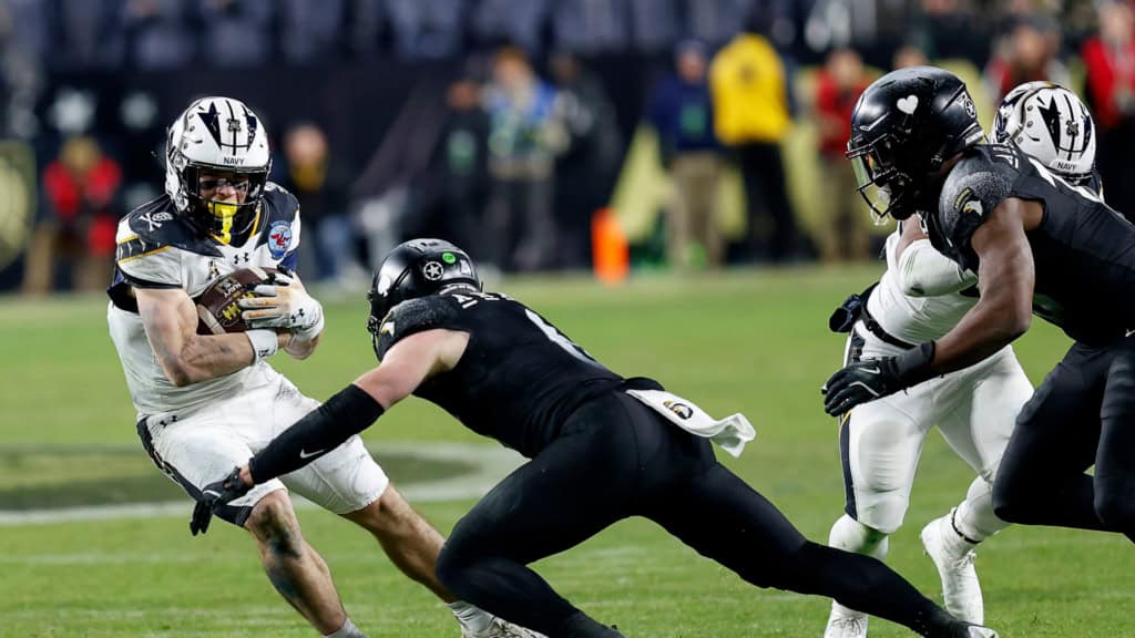 Eli Heidenreich of Navy carries the ball and tries to cut away from an Army defender during a physical run in open space.