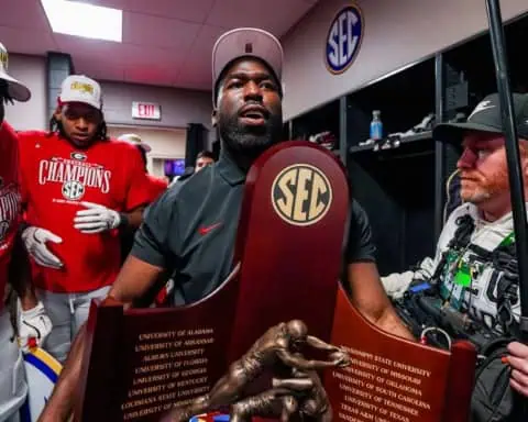 Georgia Bulldogs defensive coach celebrating with players in the locker room while holding the SEC Championship trophy after the game.