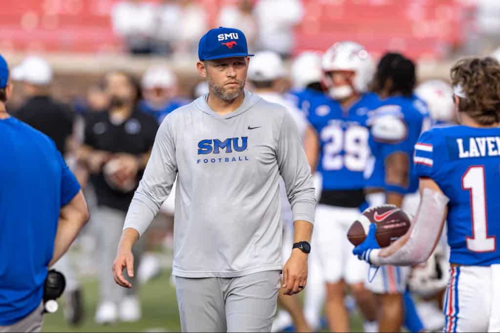SMU Mustangs defensive coach Scott Symons walking across the field during warmups while overseeing players at football practice.
