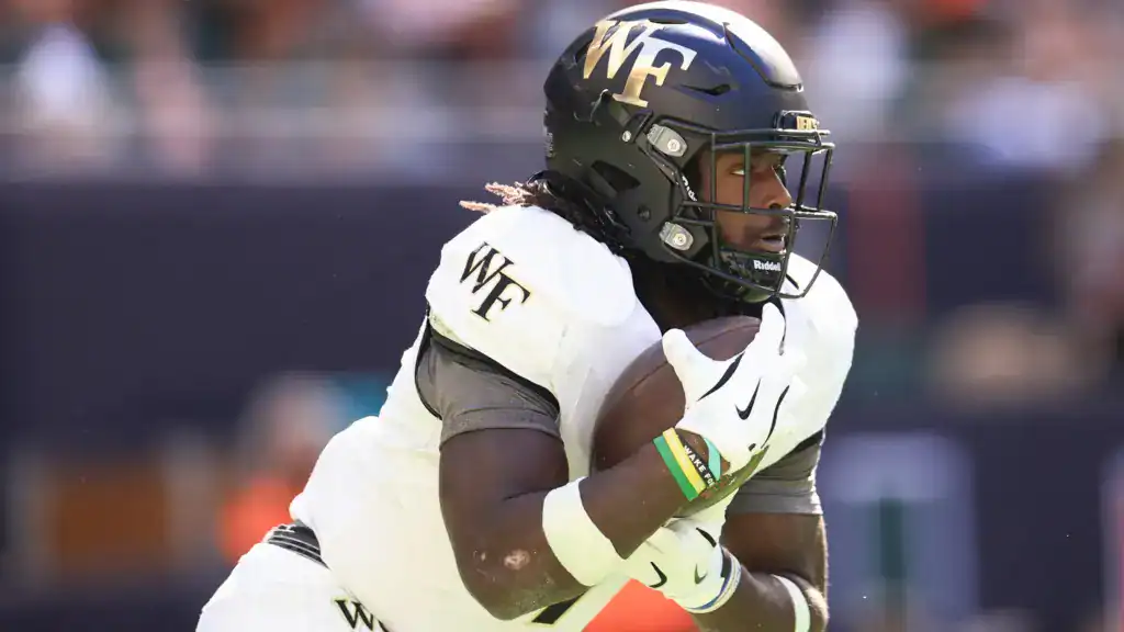 2026 NFL Draft sleeper Demond Claiborne runs with the football for Wake Forest, wearing a black helmet and white jersey in a close-up action shot.