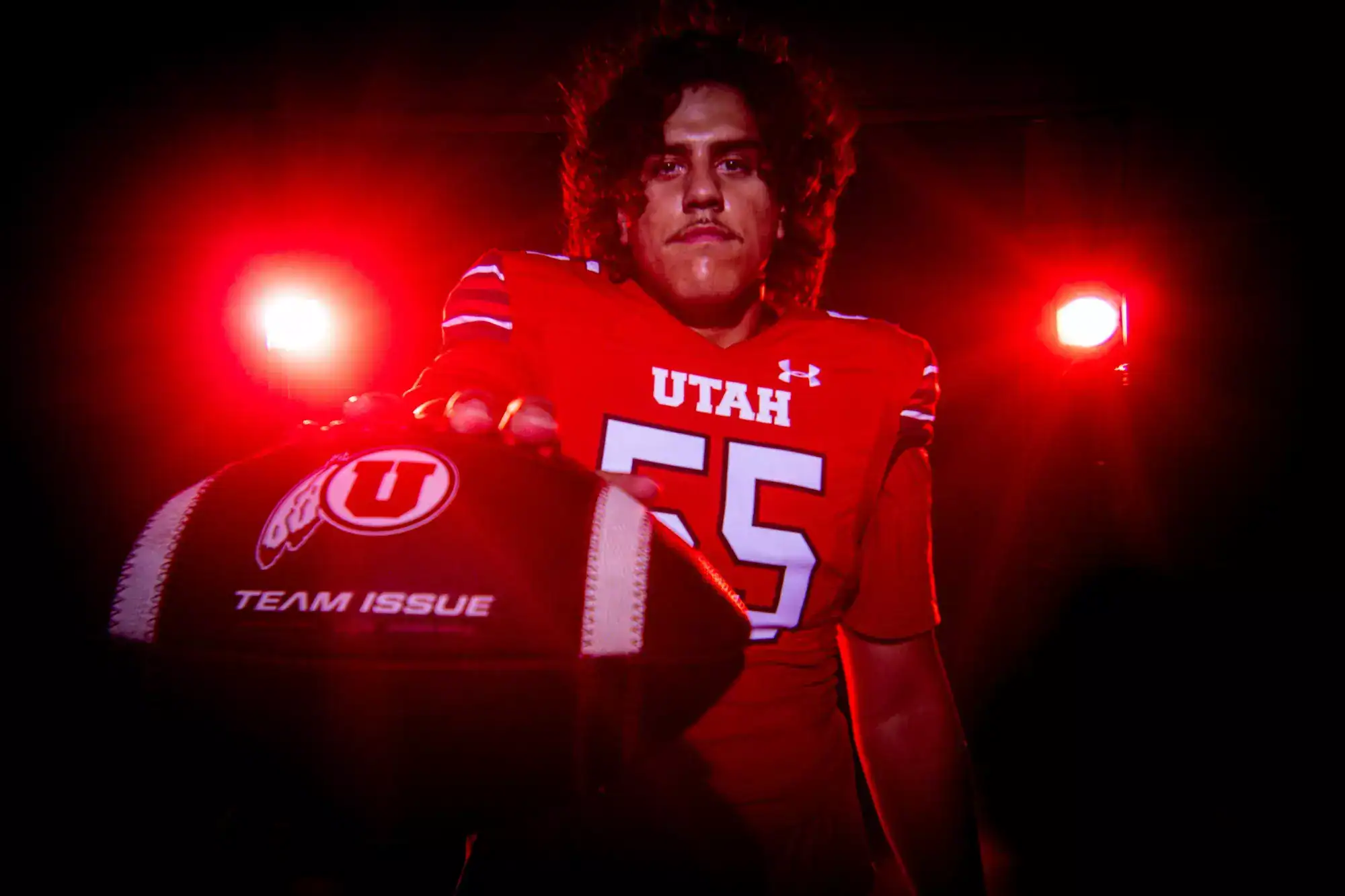 Spencer Fano, Utah offensive lineman and 2026 NFL Draft prospect, poses in a red-lit photo shoot with a football in front of him.