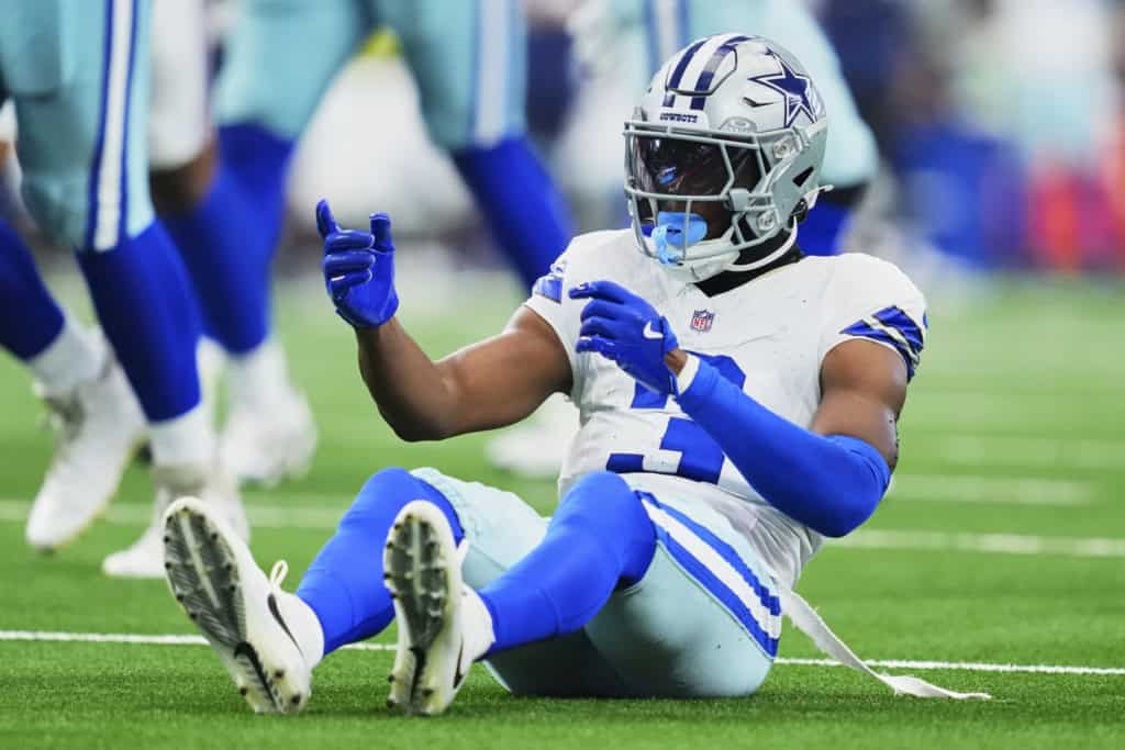 George Pickens contract extension alt text: Dallas Cowboys wide receiver George Pickens sits on the field in a white uniform and blue gloves during a game, with contract extension talk continuing around his future in Dallas.
