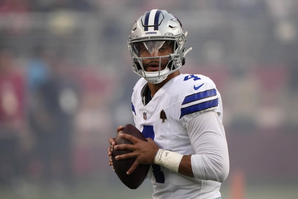 Dallas Cowboys quarterback Dak Prescott holding the football and looking downfield in his white Cowboys uniform, featured as part of the 2026 Offensive Depth Chart projection.