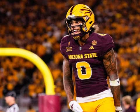 Jordyn Tyson stands on the field in Arizona State’s maroon home uniform and gold helmet during a night game.