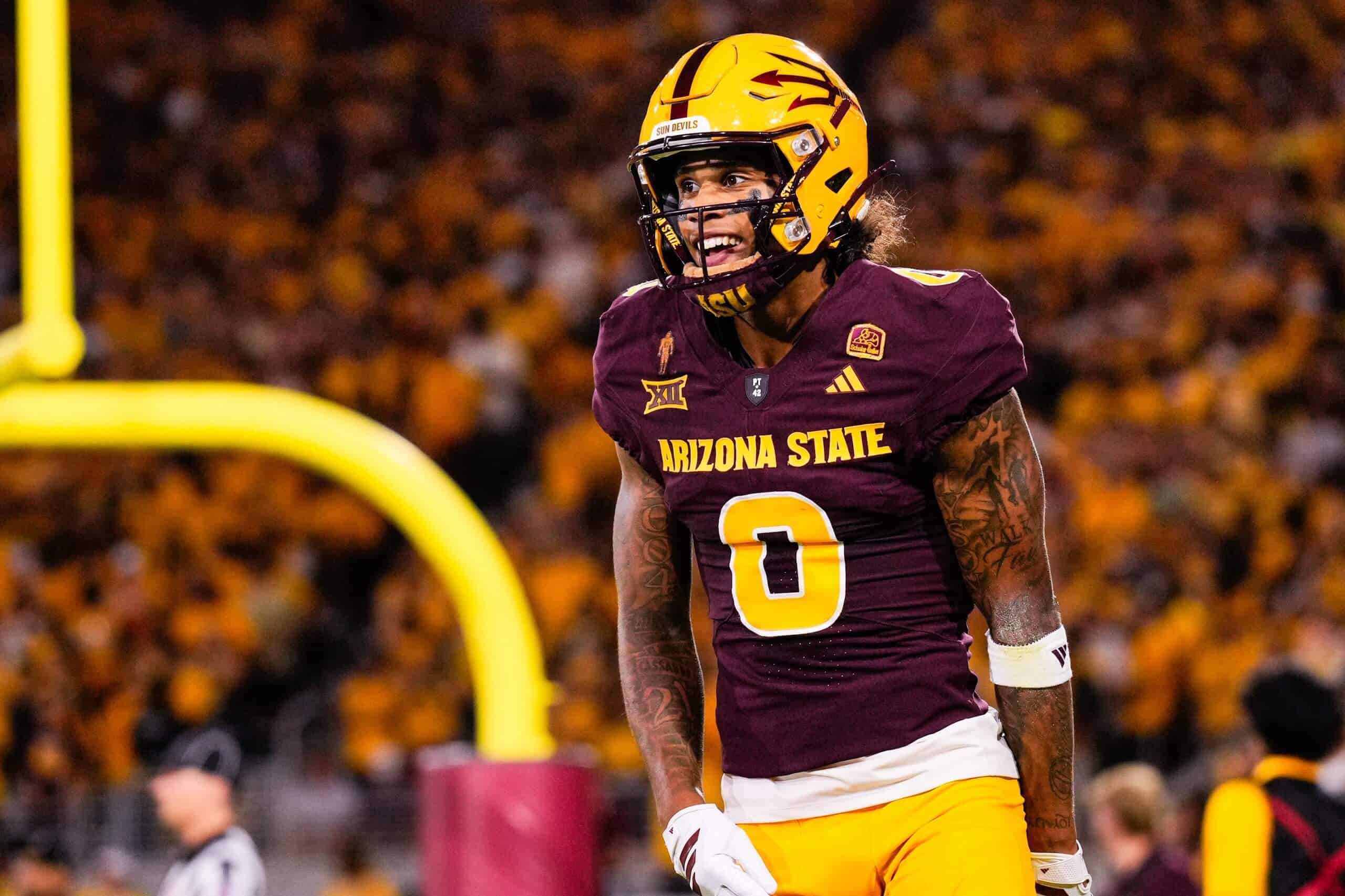 Jordyn Tyson stands on the field in Arizona State’s maroon home uniform and gold helmet during a night game.
