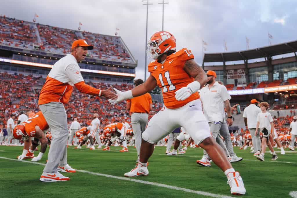 Peter Woods, Clemson draft prospect, greeting a coach on the field in an orange Tigers uniform before the game.