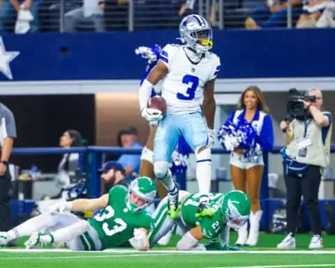 Dallas Cowboys receiver George Pickens makes a catch over two Philadelphia Eagles defenders. This shows the importance of Quinnen Williams new contract and how it affects Pickens future negotiations.