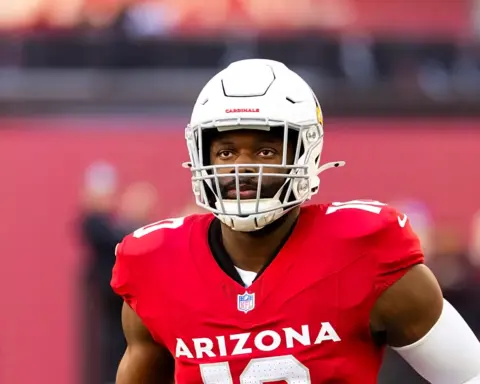 Josh Sweat looks on from the field while wearing his Arizona Cardinals helmet and red home jersey.