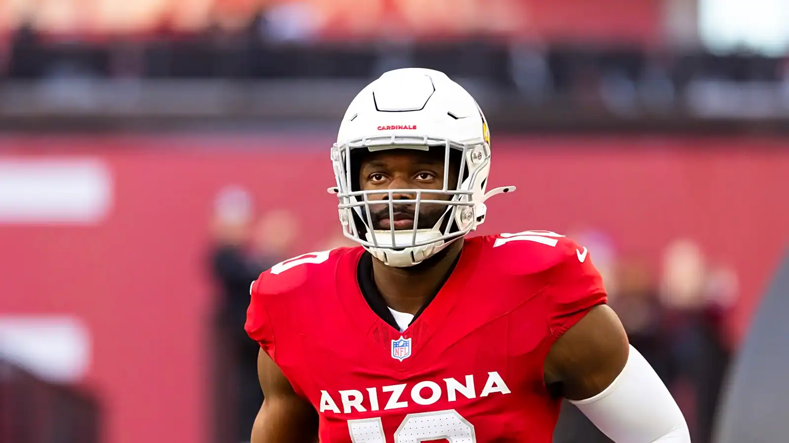 Josh Sweat looks on from the field while wearing his Arizona Cardinals helmet and red home jersey.