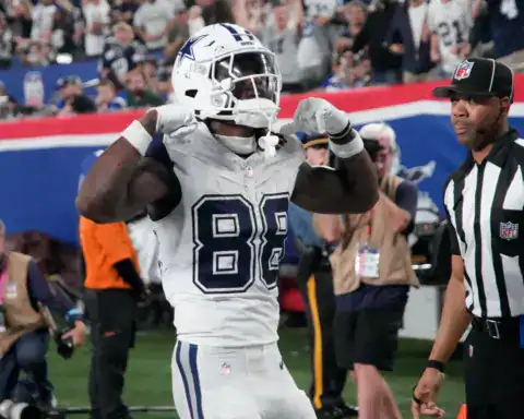 CeeDee Lamb flexing after scoring for the Dallas Cowboys in a white road uniform.