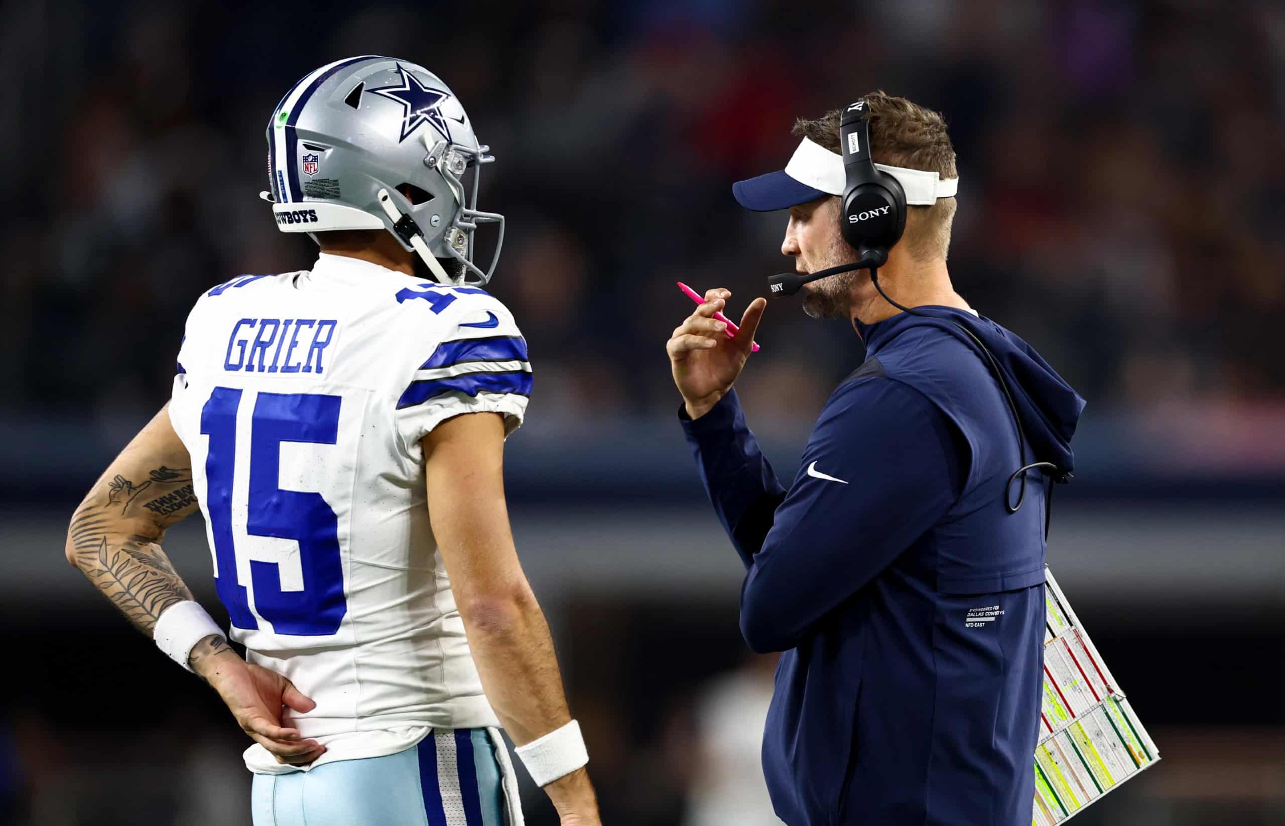 Will Grier talks with Cowboys head coach Brian Schottenheimer on the sideline during a Dallas game.