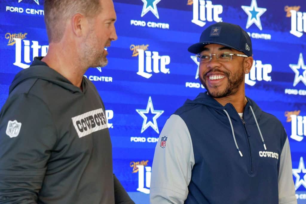 Dallas Cowboys coaches, Brian Schottenheimer and Christian Parker talk during a team event, connecting to the defensive changes that could help Dallas improve its sack production.